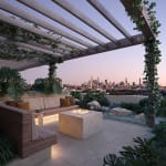 Designer rooftop BBQ area at Vera Apartments in Wooloowin, featuring a cosy firepit, lush greenery, built-in timber seating, and panoramic Brisbane city views at sunset.